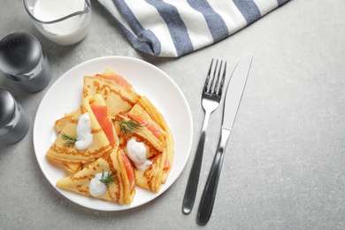 Photo of Delicious thin pancakes with salmon and sour cream on grey table, flat lay