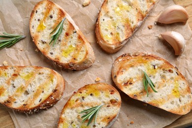 Photo of Tasty bruschettas with oil, rosemary and garlic on parchment paper, flat lay