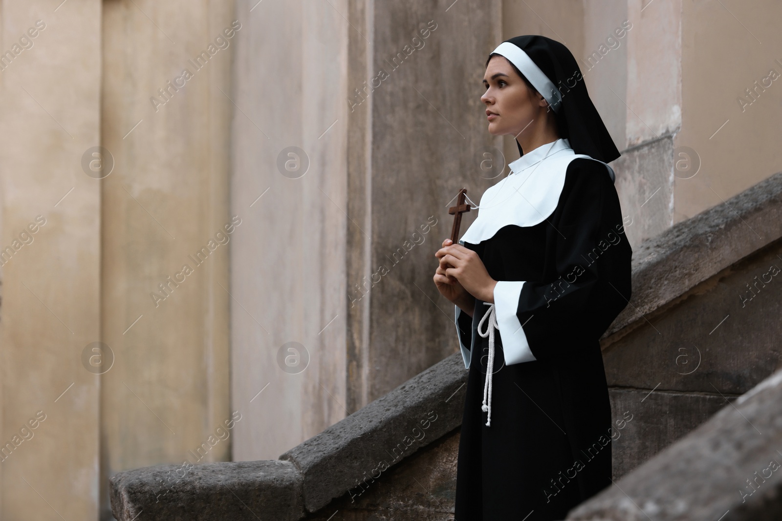 Photo of Young nun with Christian cross near building outdoors