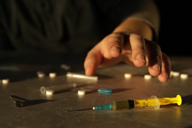 Addicted man near drugs at grey textured table, focus on syringe