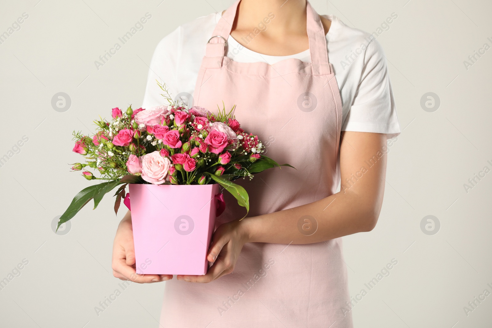 Photo of Woman holding paper gift box with flower bouquet on light background, closeup