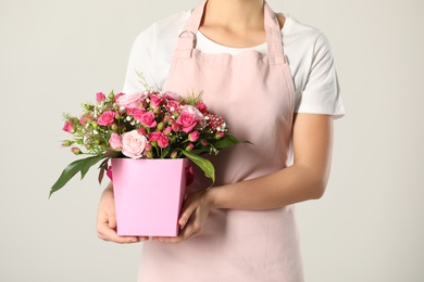 Woman holding paper gift box with flower bouquet on light background, closeup