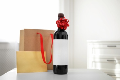 Photo of Bottle of wine, card and paper bag on table in light room. Space for text