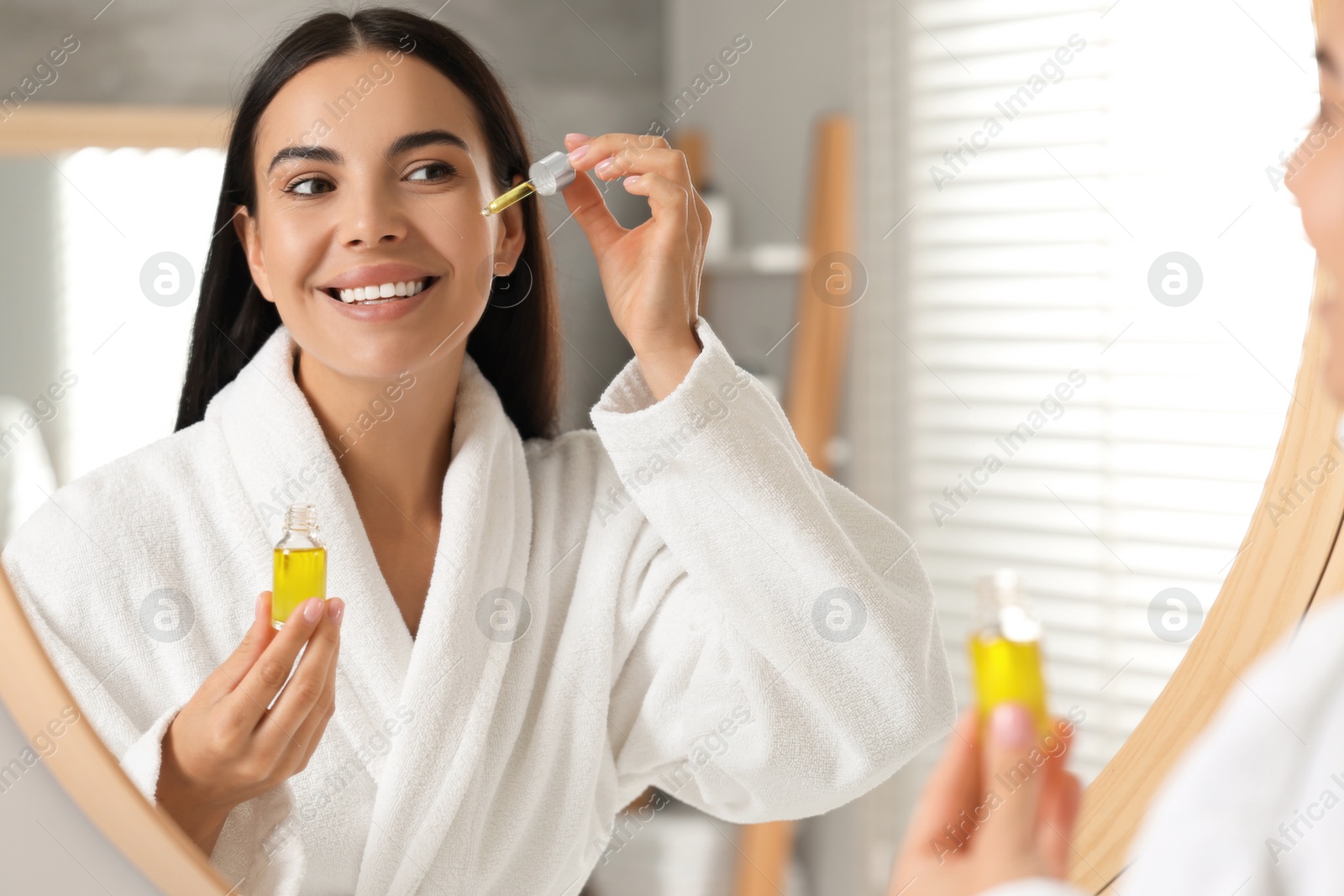 Photo of Beautiful young woman applying serum onto her face in bathroom