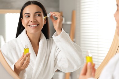 Beautiful young woman applying serum onto her face in bathroom