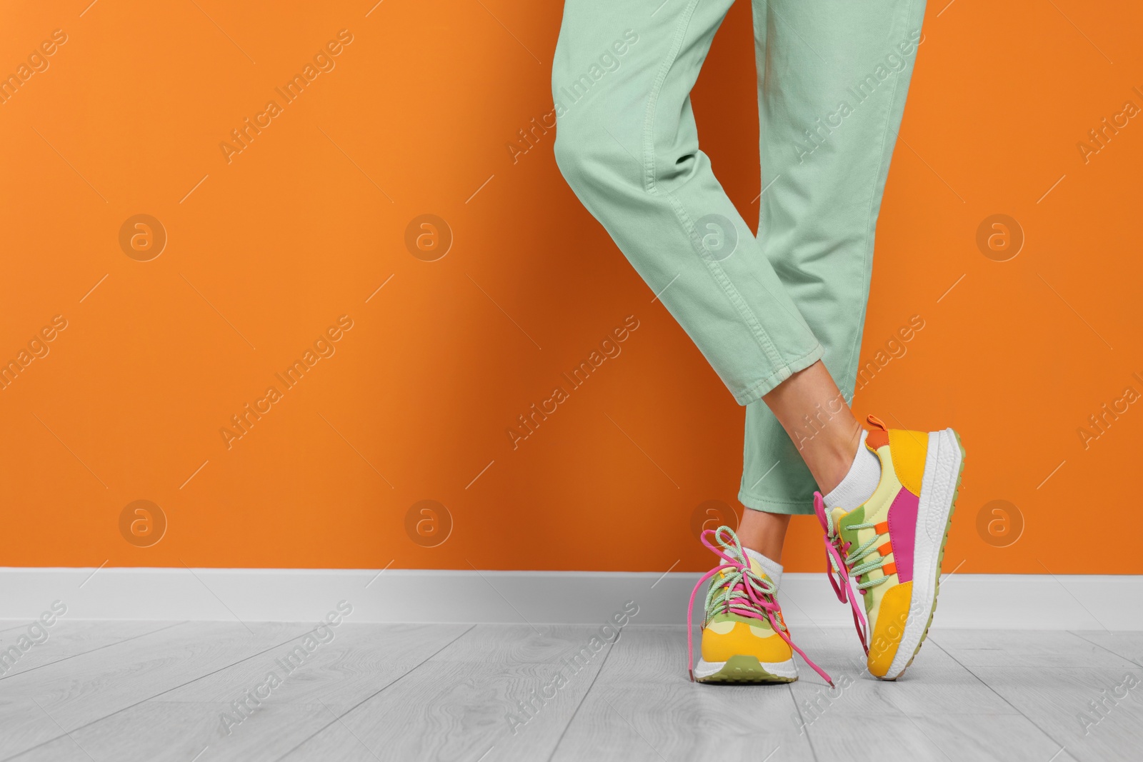 Photo of Woman wearing pair of new stylish sneakers near orange wall, closeup. Space for text