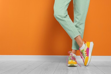 Photo of Woman wearing pair of new stylish sneakers near orange wall, closeup. Space for text