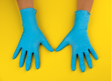 Person in medical gloves on yellow background, top view