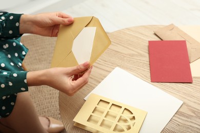 Woman holding greeting card at wooden table in living room, closeup