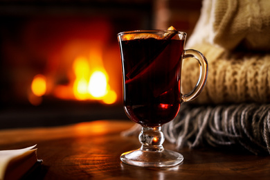 Photo of Tasty mulled wine, book, knitwear and blurred fireplace on background