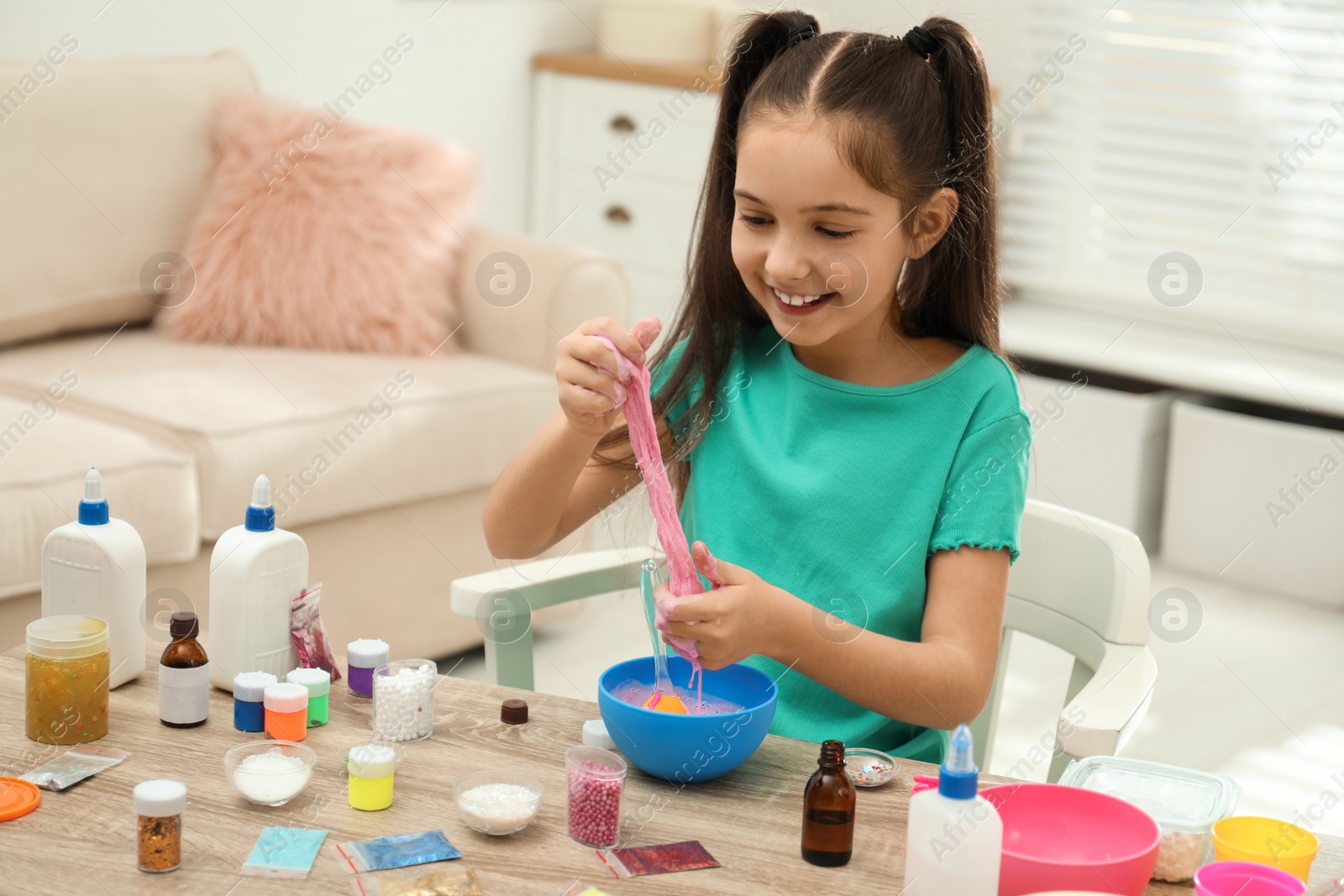 Photo of Cute little girl making DIY slime toy at table indoors