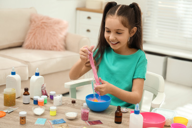 Photo of Cute little girl making DIY slime toy at table indoors