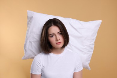 Photo of Unhappy young woman with pillow on beige background. Insomnia problem