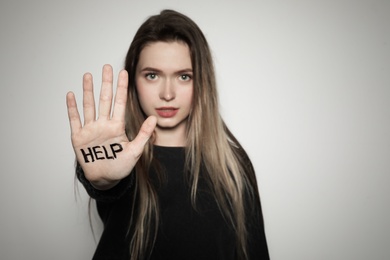 Young woman with word HELP written on her palm against light background, focus on hand. Space for text