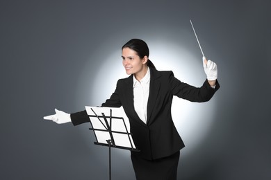 Photo of Happy professional conductor with baton and note stand on grey background
