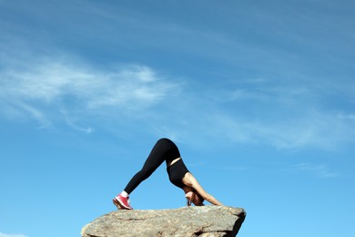 Beautiful young woman practicing yoga on rock in mountains