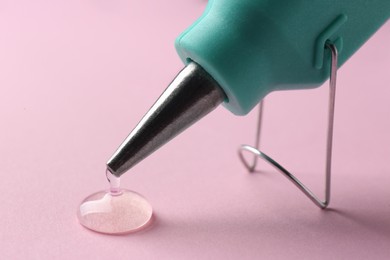 Photo of Melted glue dripping out of hot gun nozzle on pink background, closeup
