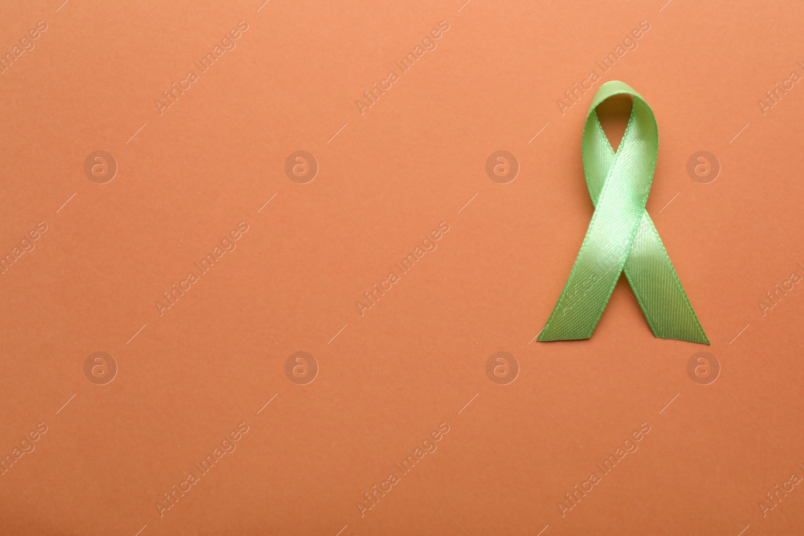 Photo of World Mental Health Day. Green ribbon on pale orange background, top view with space for text