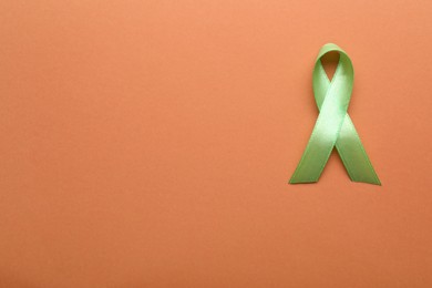 World Mental Health Day. Green ribbon on pale orange background, top view with space for text