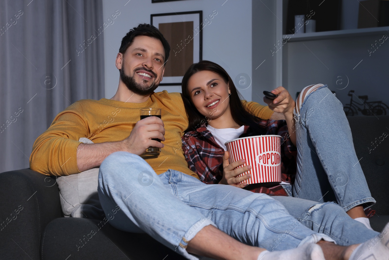 Photo of Happy couple with popcorn watching TV at home in evening