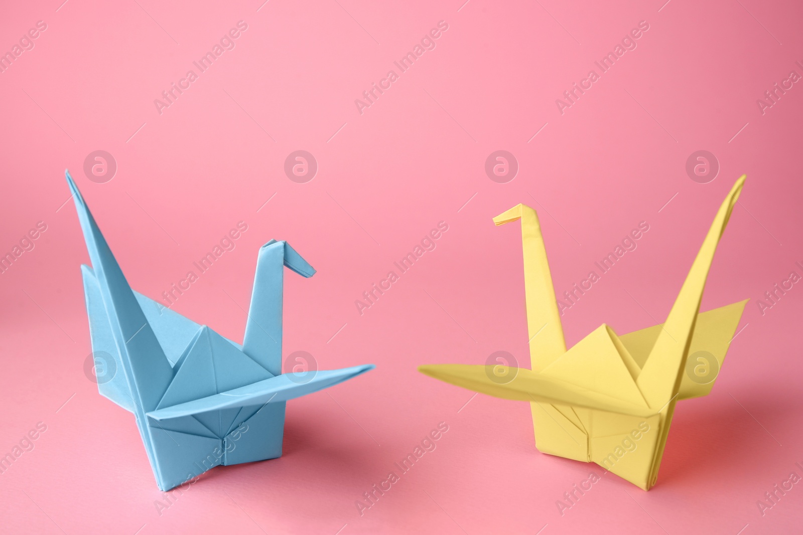 Photo of Origami art. Colorful handmade paper cranes on pink background