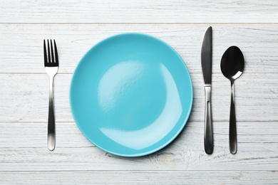 Stylish ceramic plate and cutlery on white wooden background, flat lay