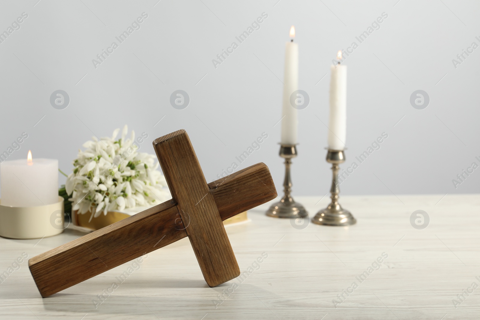 Photo of Burning church candles, wooden cross and flowers on white table. Space for text