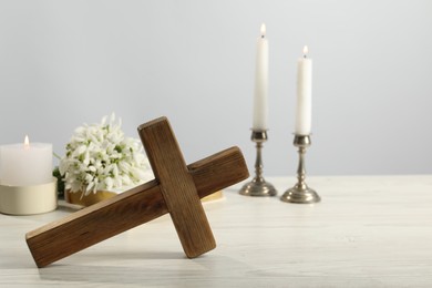 Burning church candles, wooden cross and flowers on white table. Space for text