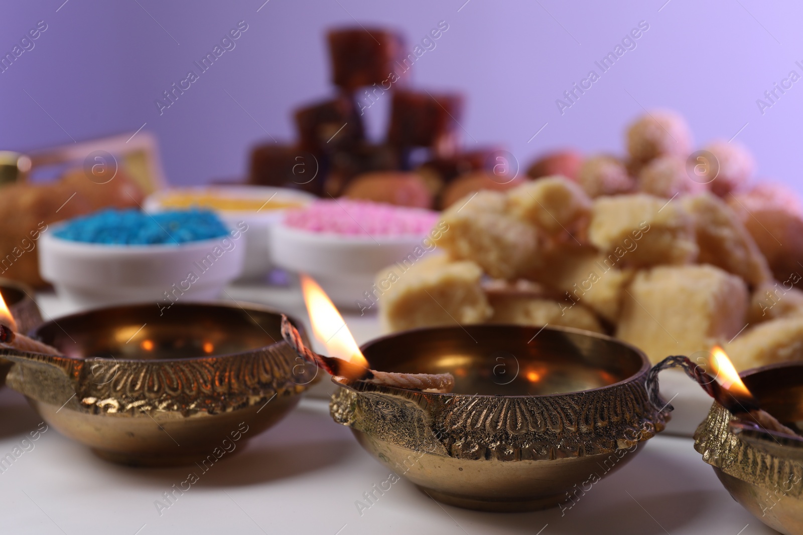 Photo of Happy Diwali. Diya lamps on white table against violet background, closeup