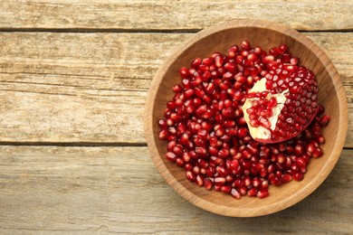 Ripe juicy pomegranate grains in bowl on wooden table, top view. Space for text