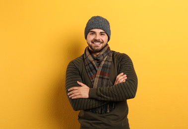 Happy young man in warm clothes on yellow background. Winter vacation