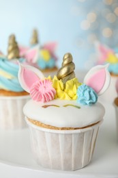 Photo of Cute sweet unicorn cupcakes on white table, closeup