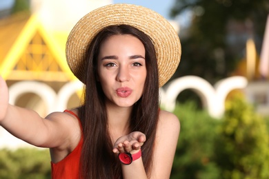 Photo of Happy young woman in stylish hat taking selfie outdoors on sunny day