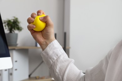 Man squeezing yellow stress ball in office, closeup