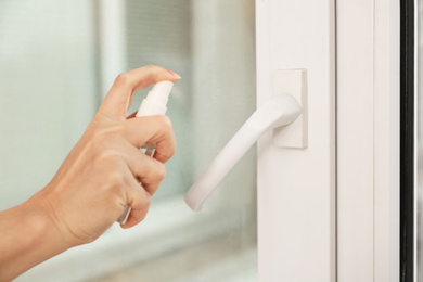 Photo of Woman spraying antiseptic onto window handle indoors, closeup