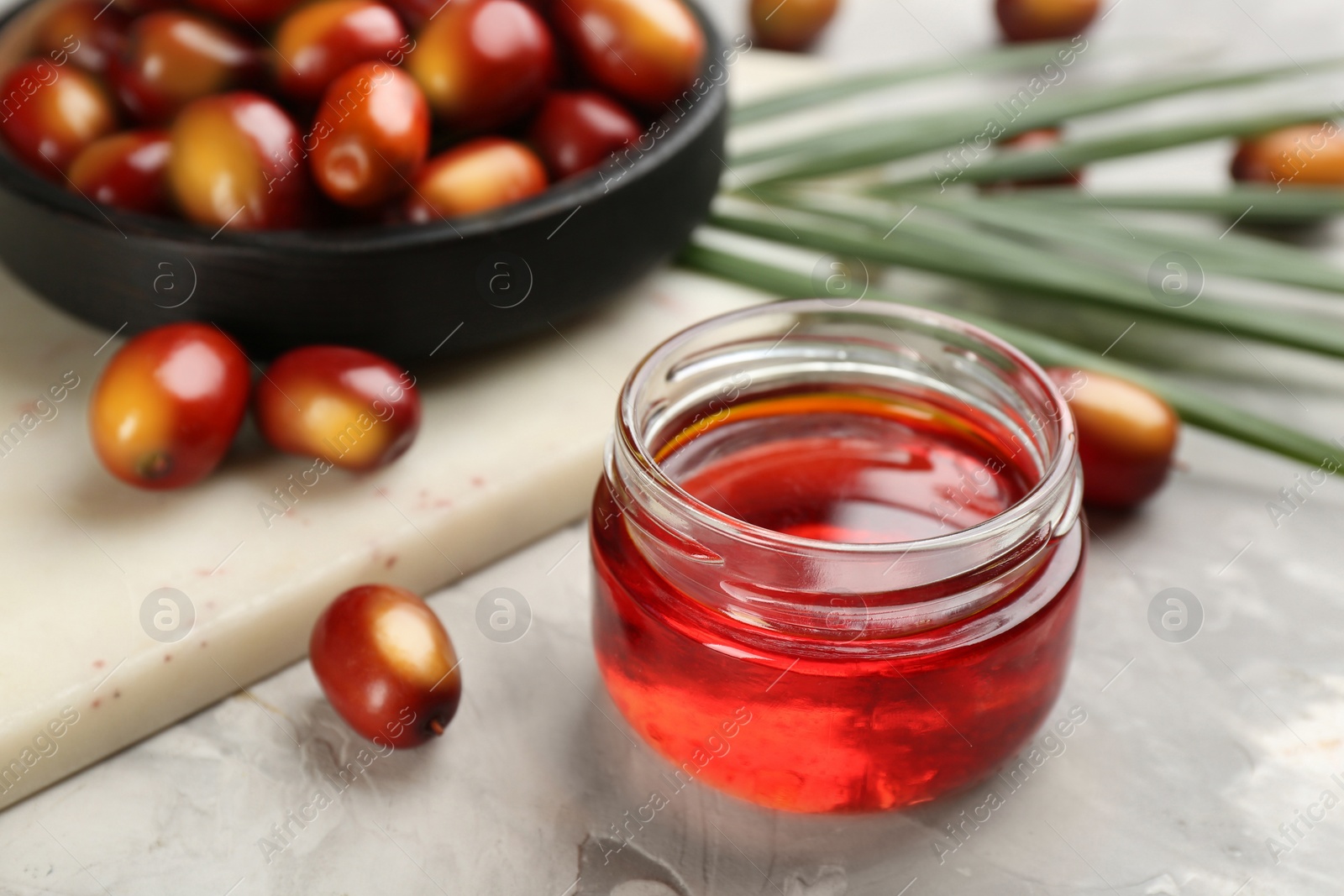 Photo of Palm oil in glass jar, tropical leaf and fruits on grey table