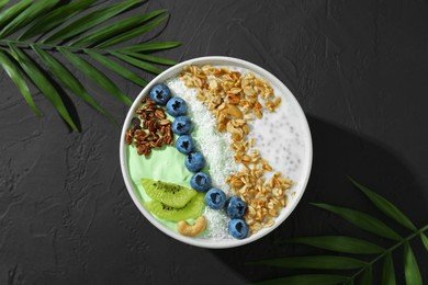 Photo of Tasty smoothie bowl with fresh kiwi fruit, blueberries and oatmeal on black table, flat lay