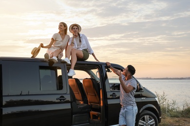 Photo of Happy friends near sea at sunset. Summer trip