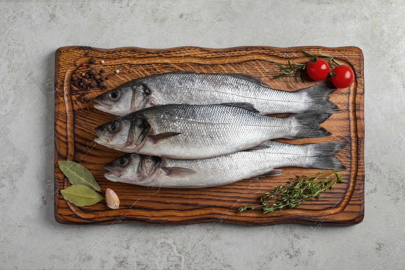 Photo of Tasty sea bass fish with spices on grey textured table, top view