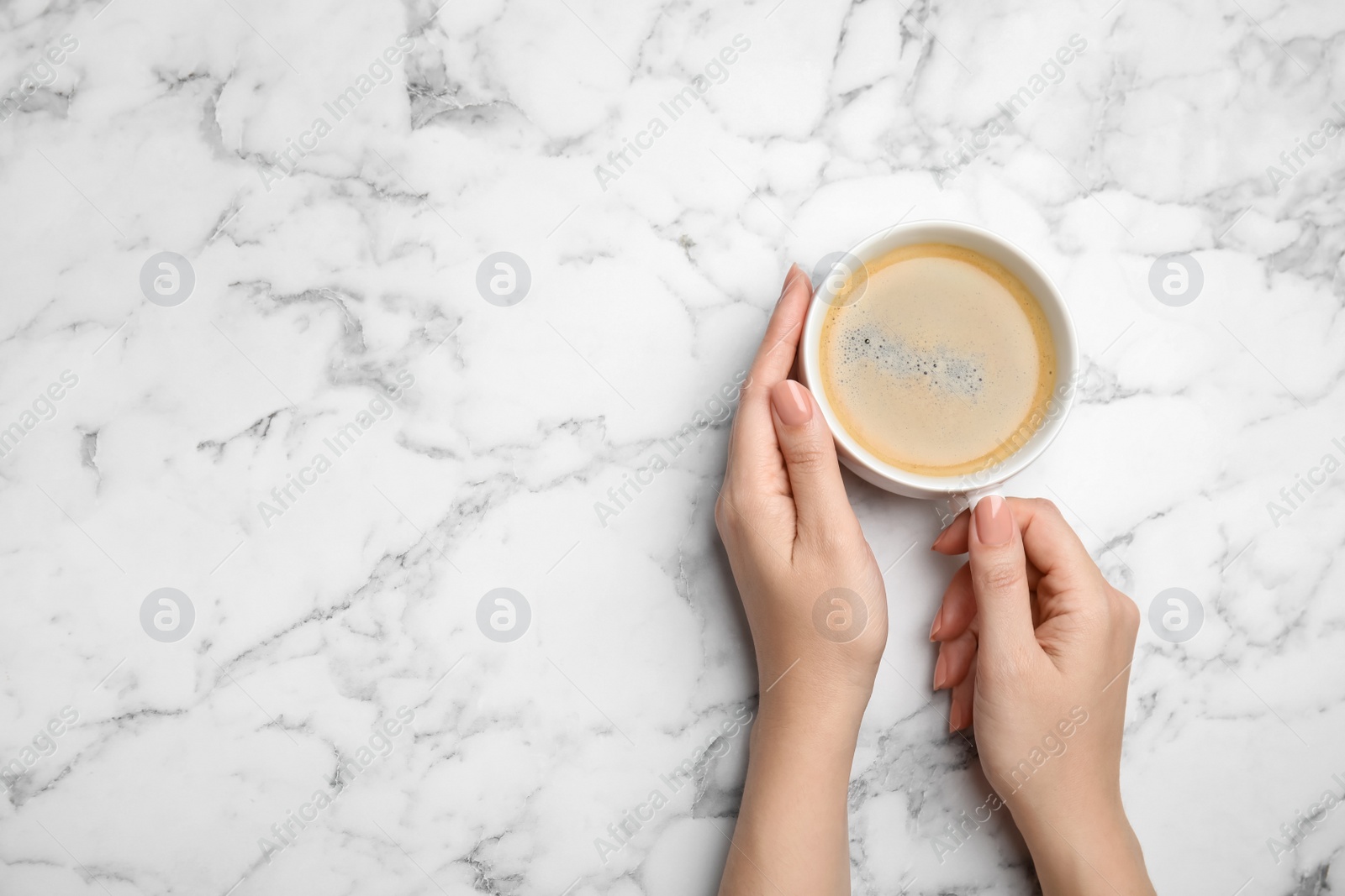 Photo of Woman with cup of coffee at white marble table, top view. Space for text