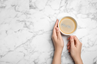 Photo of Woman with cup of coffee at white marble table, top view. Space for text