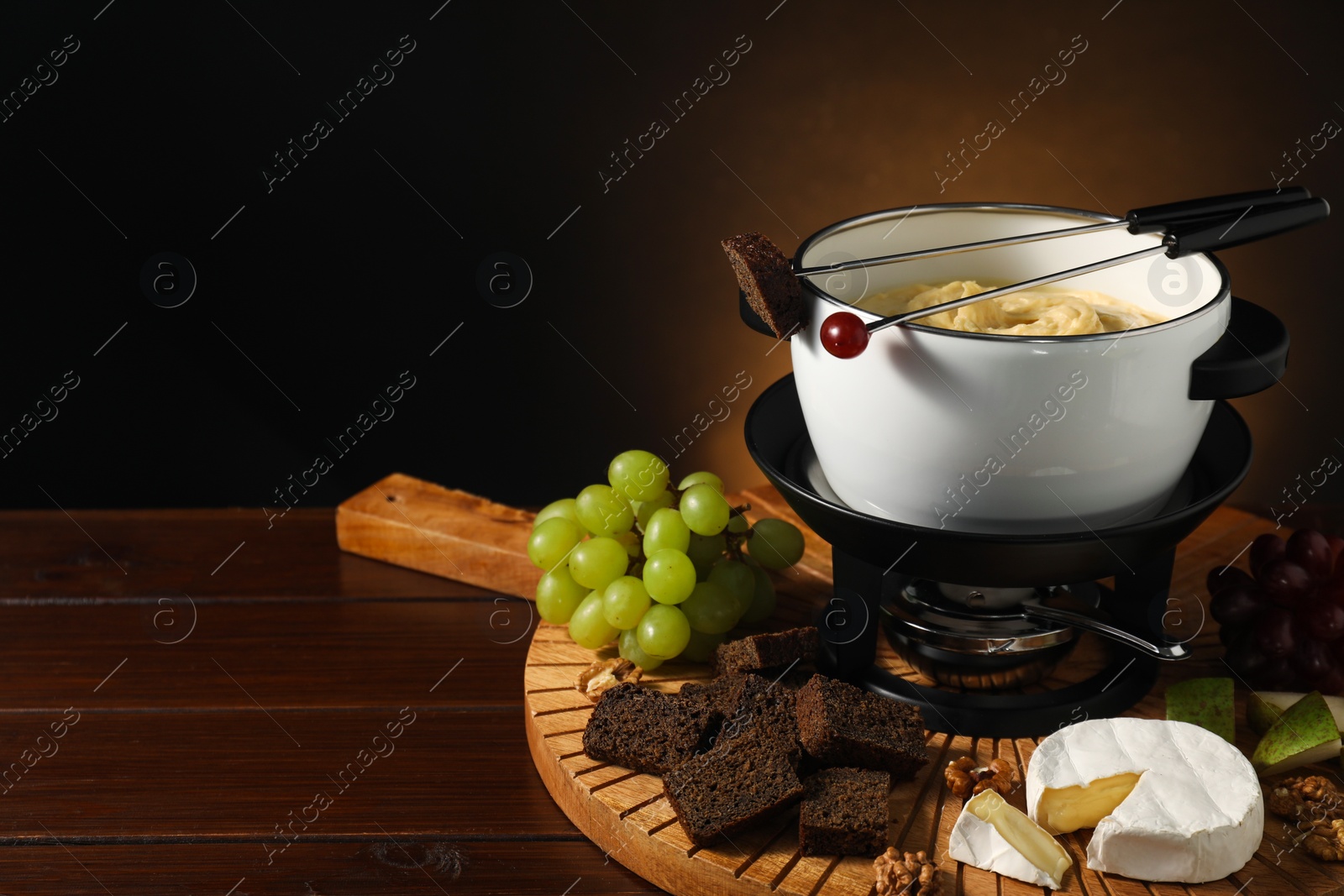 Photo of Forks with pieces of grape, bread, fondue pot with melted cheese and snacks on wooden table, closeup. Space for text