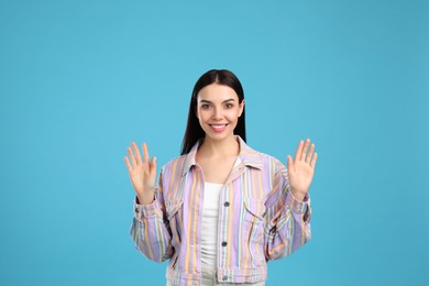 Photo of Attractive young woman showing hello gesture on light blue background