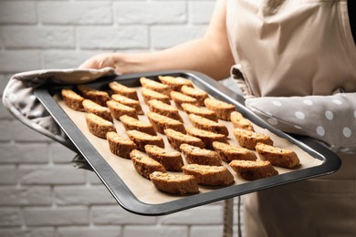 Photo of Woman holding baking tray with tasty cantucci indoors, closeup. Traditional Italian almond biscuits