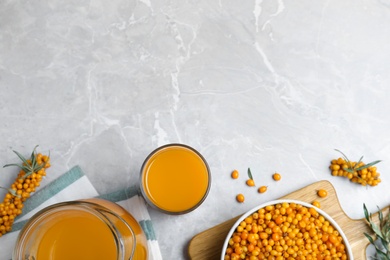 Photo of Sea buckthorn juice and fresh berries on light marble table, flat lay. Space for text