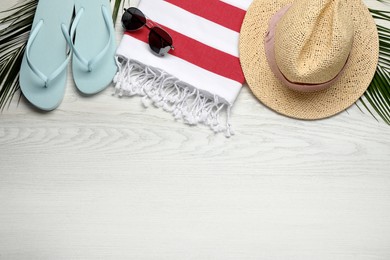 Beach towel, flip flops, sunglasses and straw hat on white wooden background, flat lay. Space for text