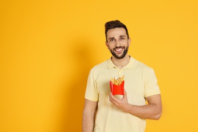 Man with French fries on yellow background, space for text