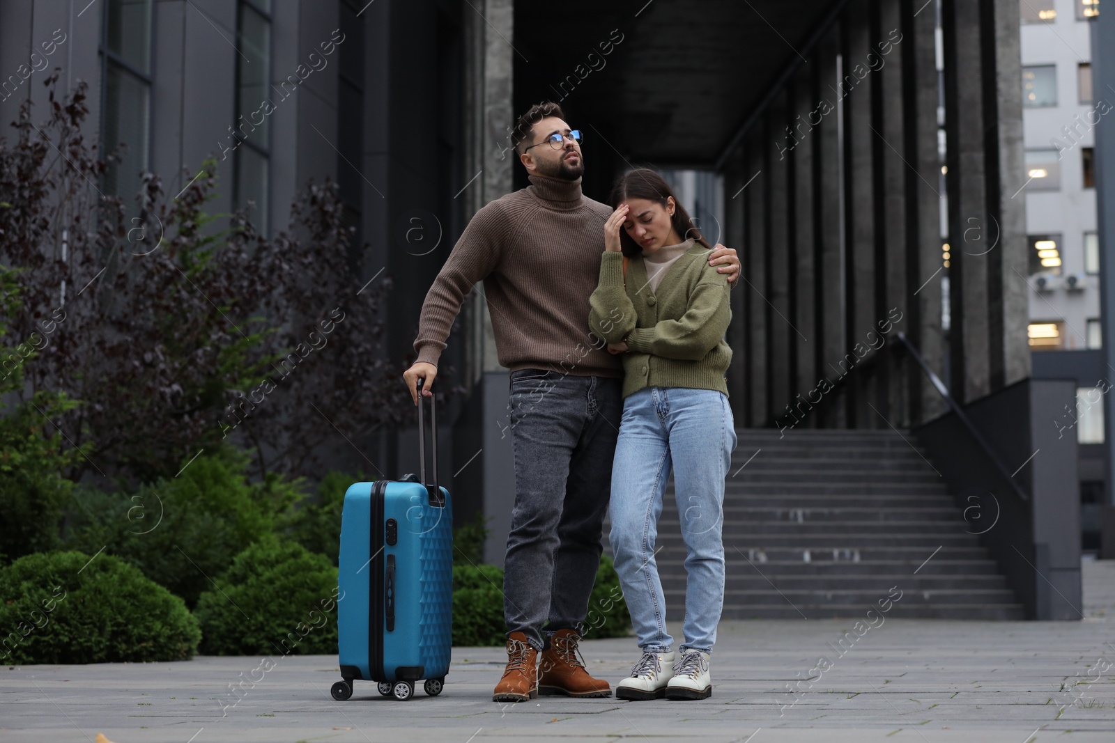 Photo of Being late. Worried couple with suitcase near building outdoors