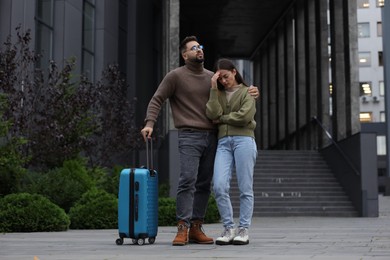 Photo of Being late. Worried couple with suitcase near building outdoors