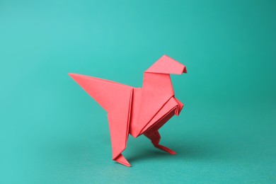 Photo of Origami art. Handmade red paper dinosaur on turquoise background